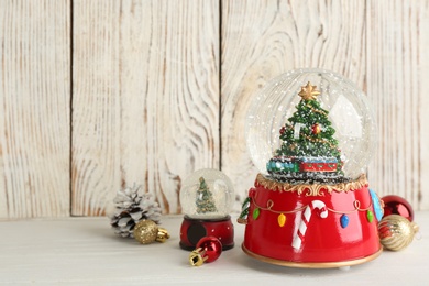 Beautiful snow globes and Christmas decor on light wooden table, space for text