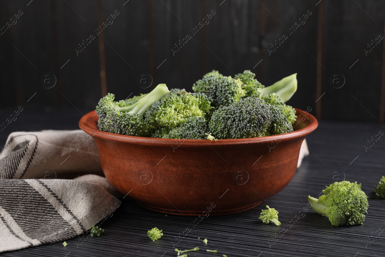 Photo of Bowl with fresh raw broccoli on black wooden table