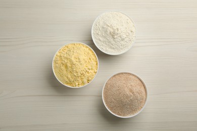 Photo of Different types of flours in bowls on white wooden table, flat lay