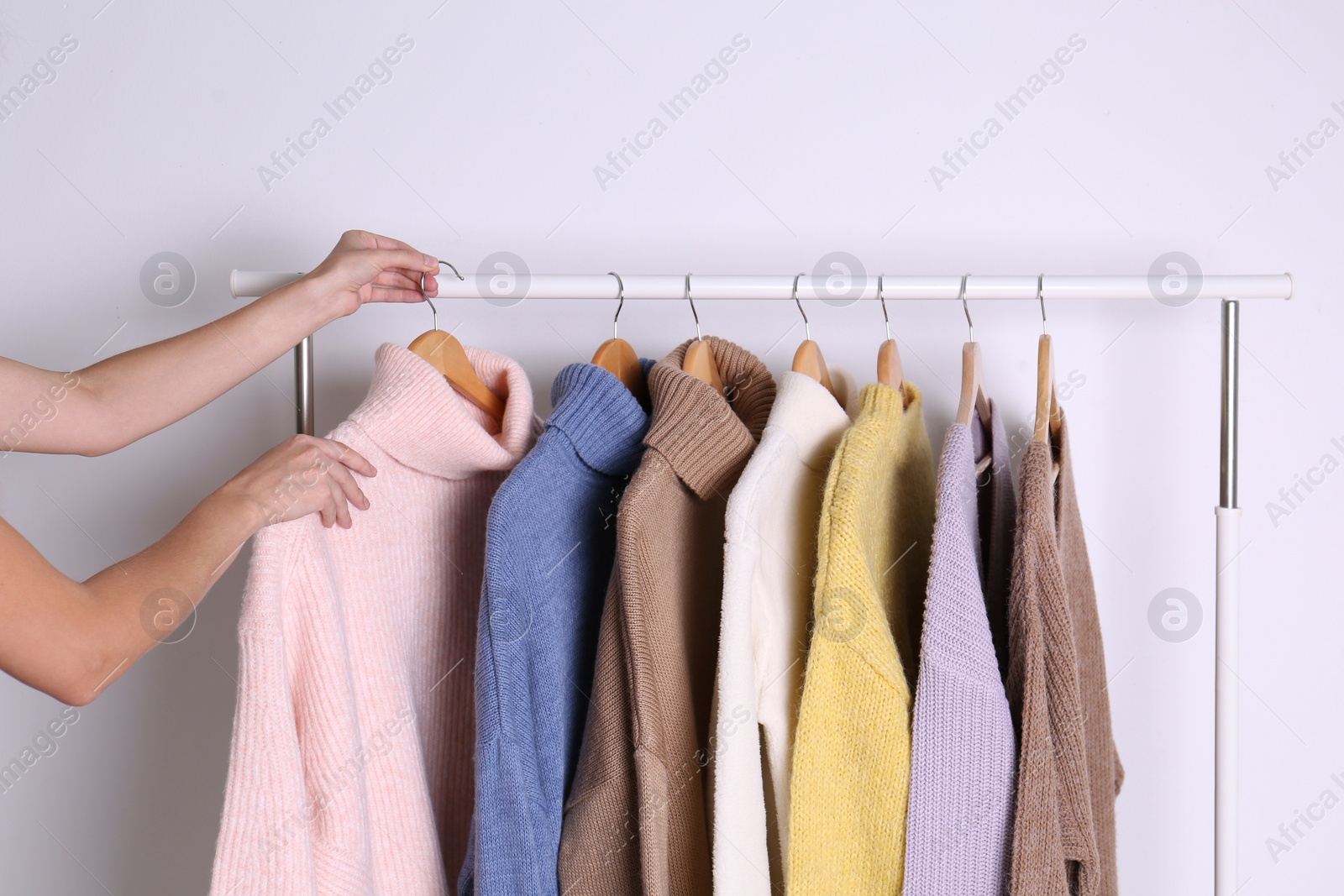 Photo of Woman choosing sweater on rack against white background, closeup