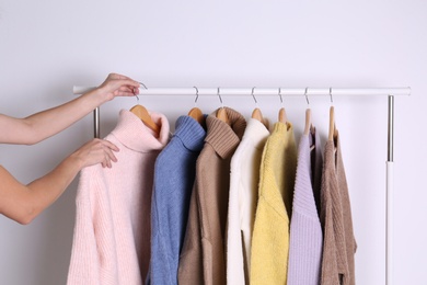 Photo of Woman choosing sweater on rack against white background, closeup