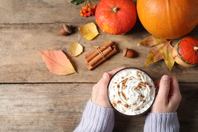 Photo of Woman with glass cup of tasty pumpkin spice latte at wooden table, top view