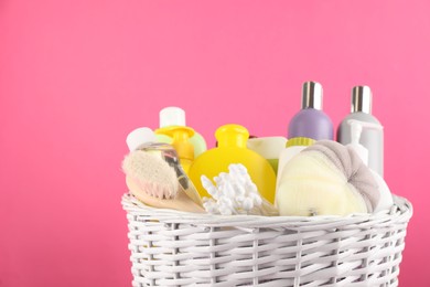Photo of Different baby cosmetic products and bathing accessories in wicker basket on pink background, closeup. Space for text