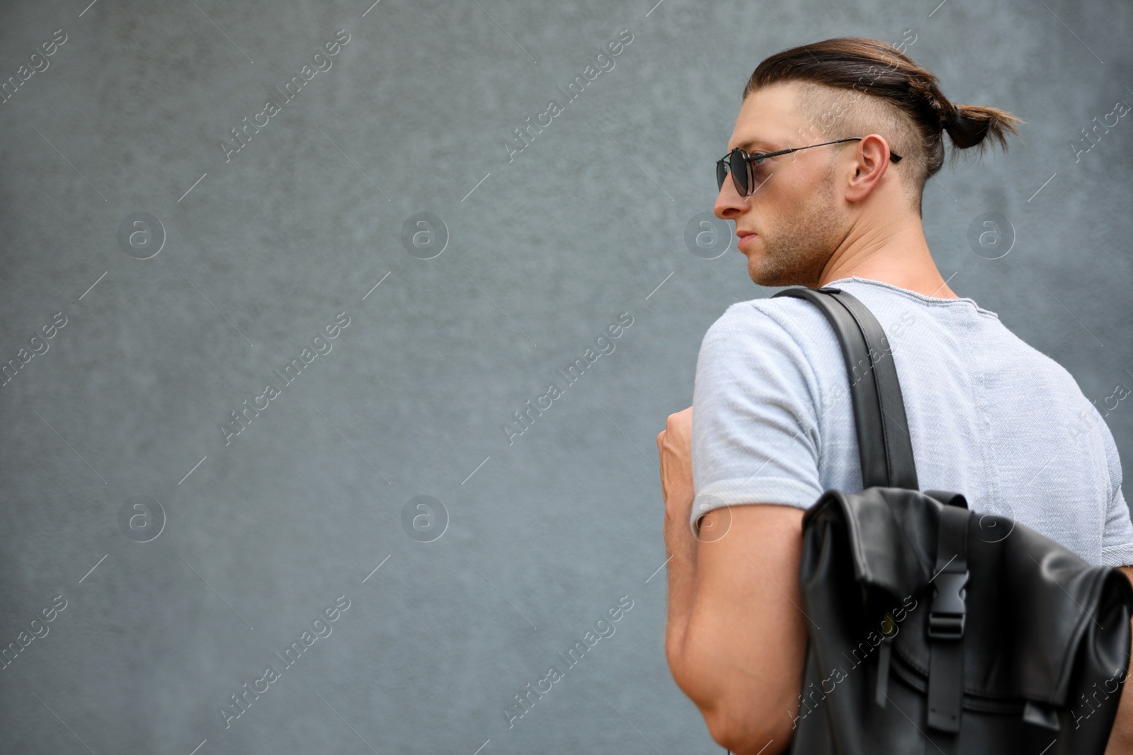 Photo of Handsome young man in stylish sunglasses with backpack near grey wall, space for text