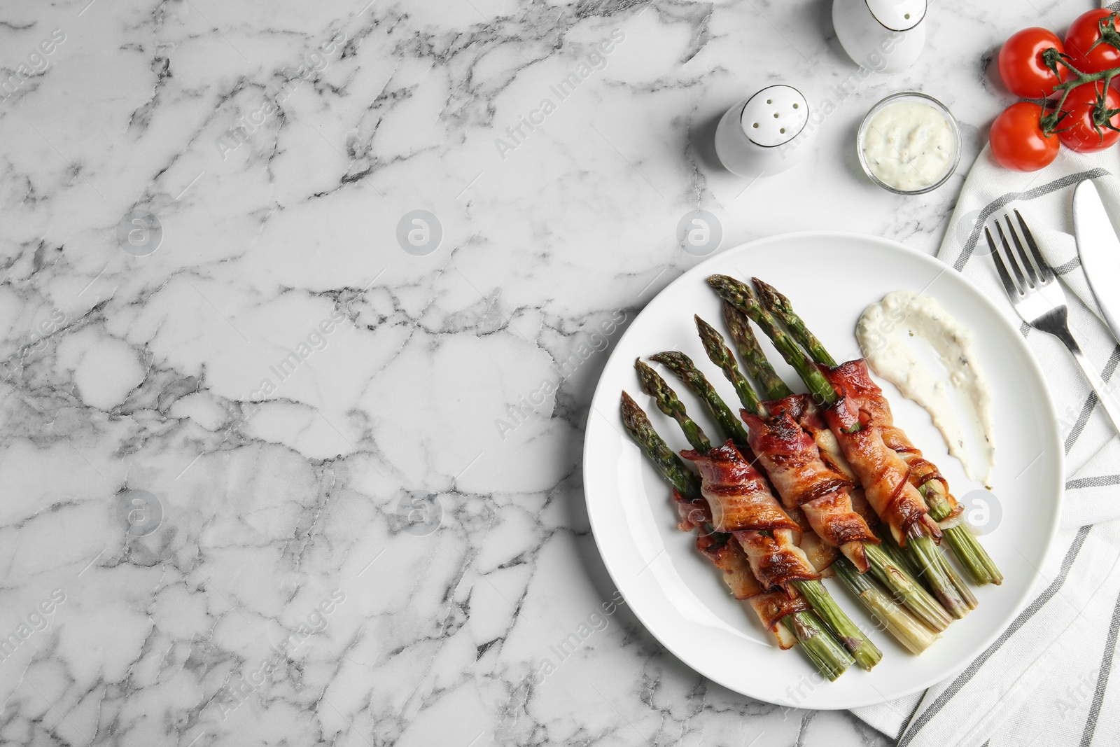 Photo of Oven baked asparagus wrapped with bacon on white marble table, flat lay. Space for text