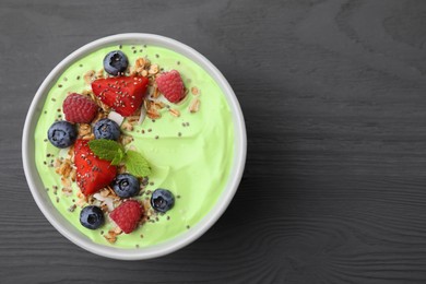 Photo of Tasty matcha smoothie bowl served with berries and oatmeal on grey wooden table, top view with space for text. Healthy breakfast