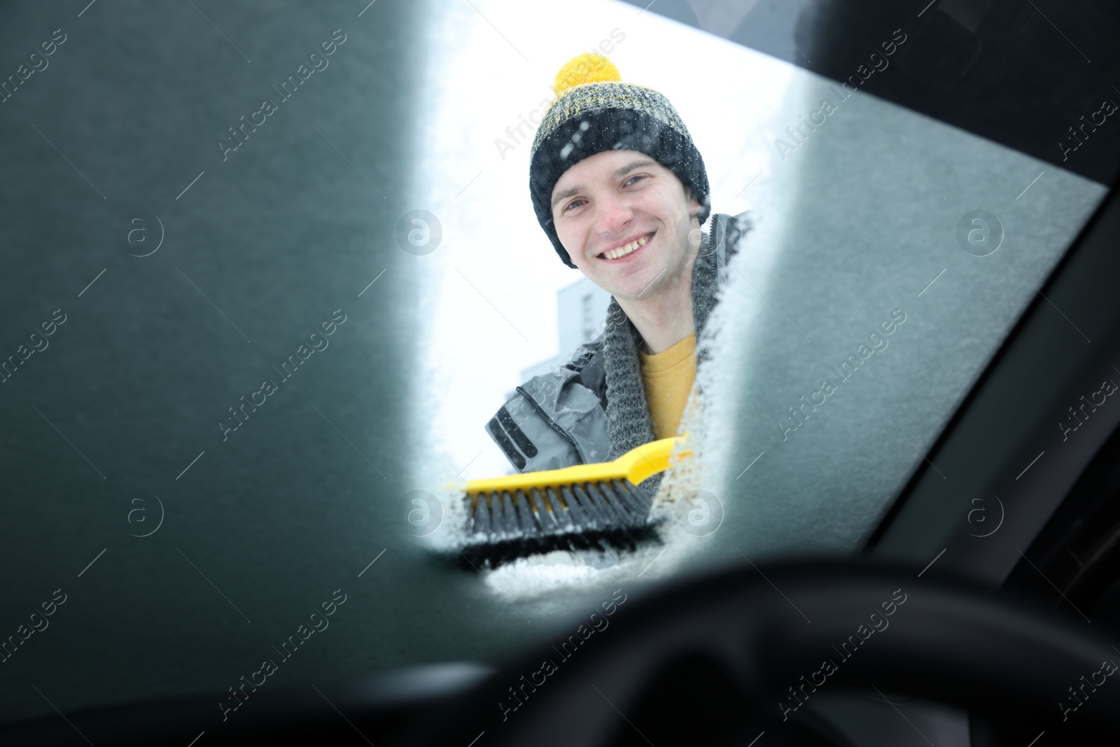 Photo of Man cleaning snow from car windshield, view from inside