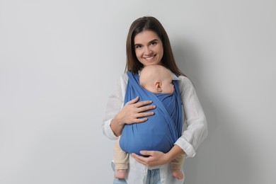 Photo of Mother holding her child in sling (baby carrier) on light grey background