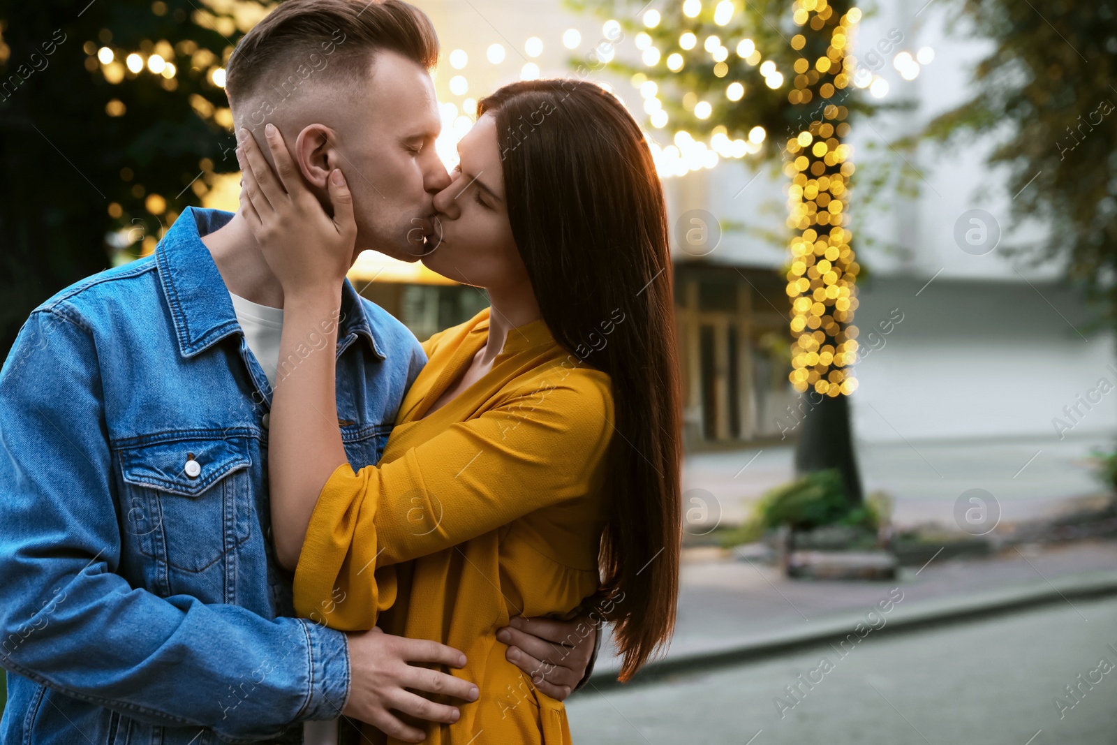 Photo of Happy young couple kissing on city street, space for text