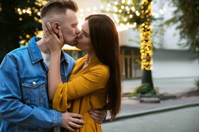 Happy young couple kissing on city street, space for text