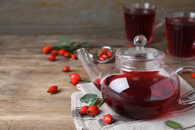 Photo of Teapot with aromatic rose hip tea and fresh berries on wooden table, space for text