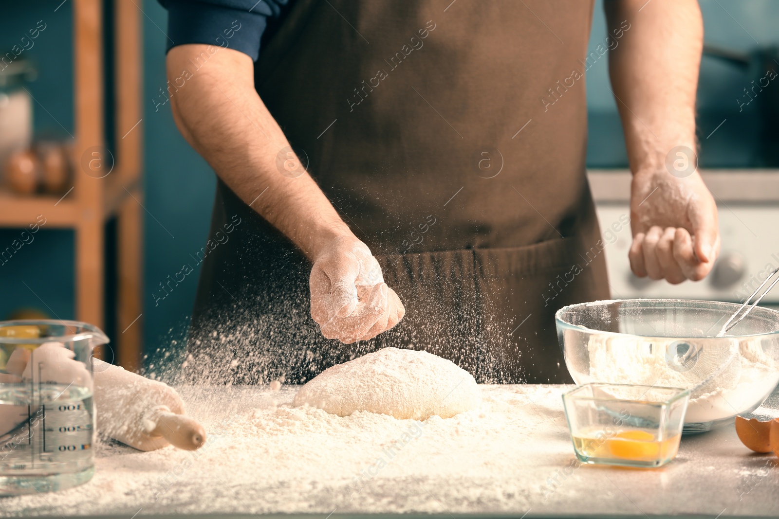 Photo of Man sprinkling flour over dough on table in kitchen