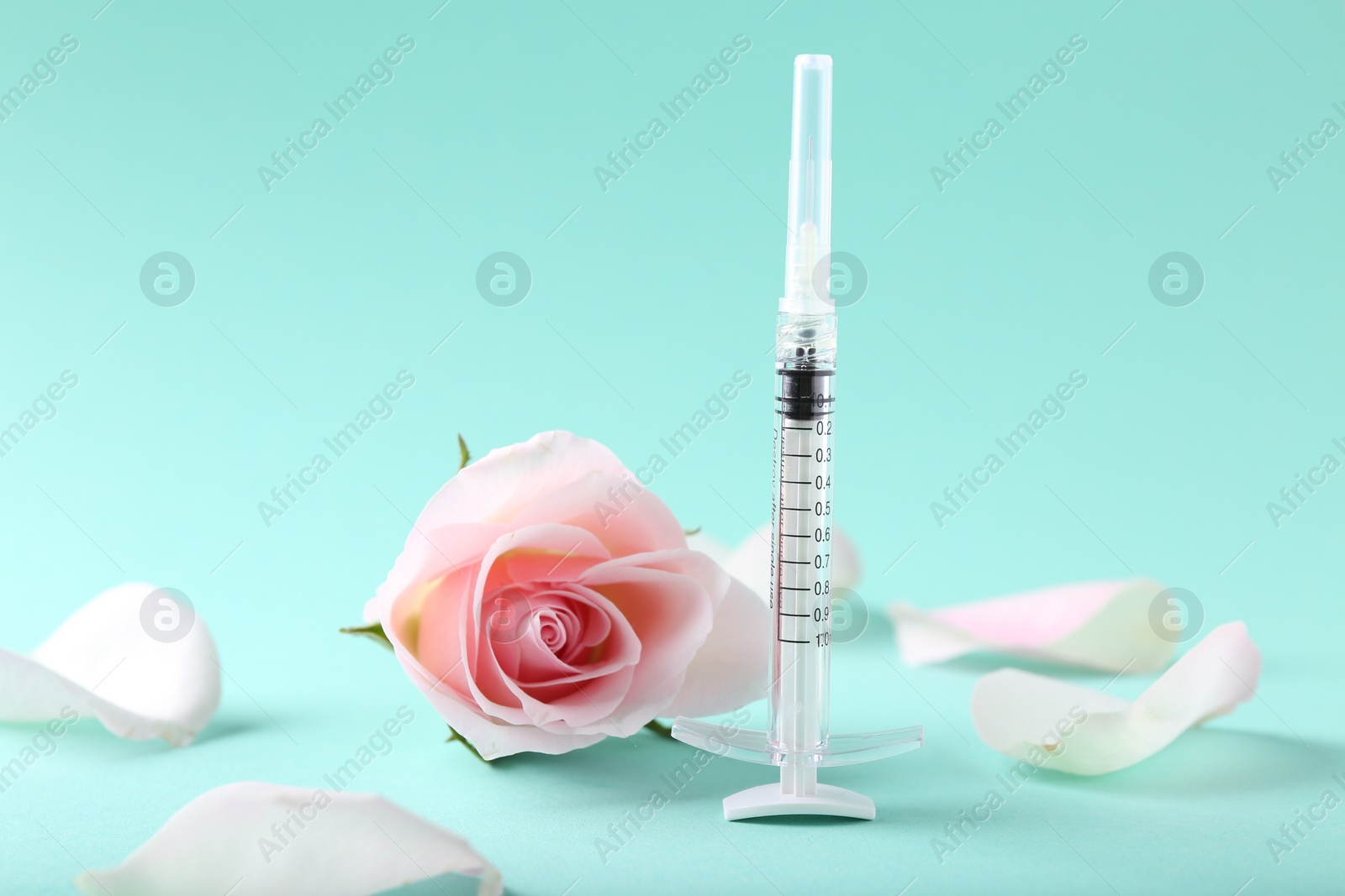 Photo of Cosmetology. Medical syringe, rose flower and petals on turquoise background