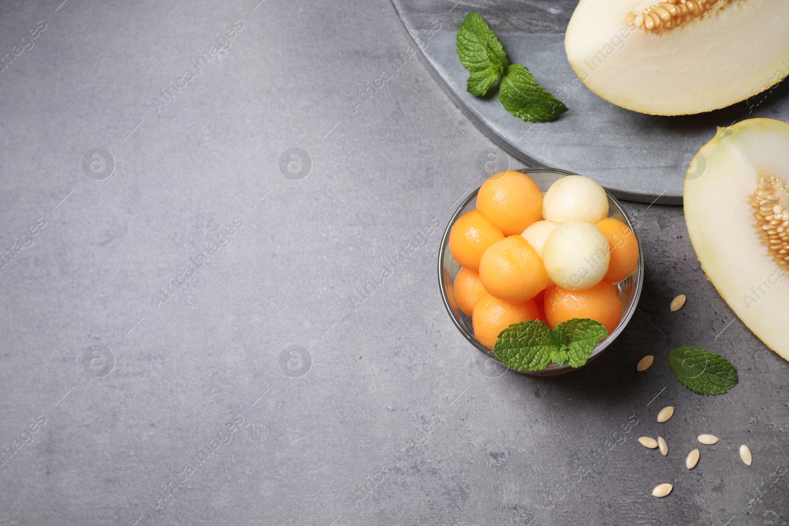 Photo of Melon balls and mint in glass on grey table, flat lay. Space for text