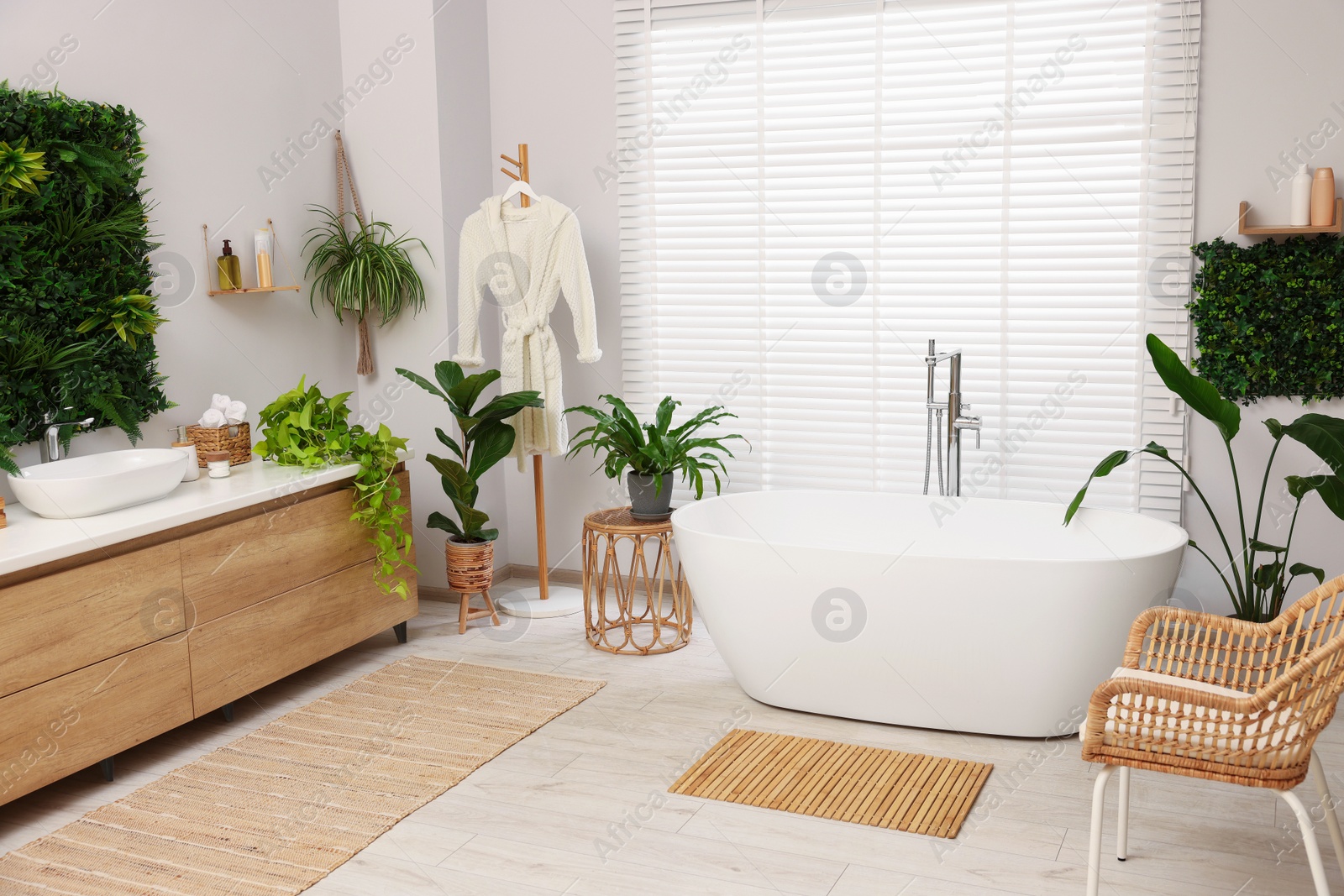 Photo of Green artificial plants, vanity and tub in bathroom
