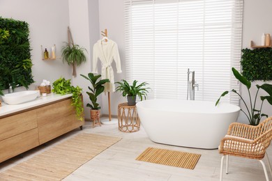 Photo of Green artificial plants, vanity and tub in bathroom