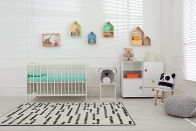 Photo of Comfortable crib near wall with color shelves in baby room. Interior design