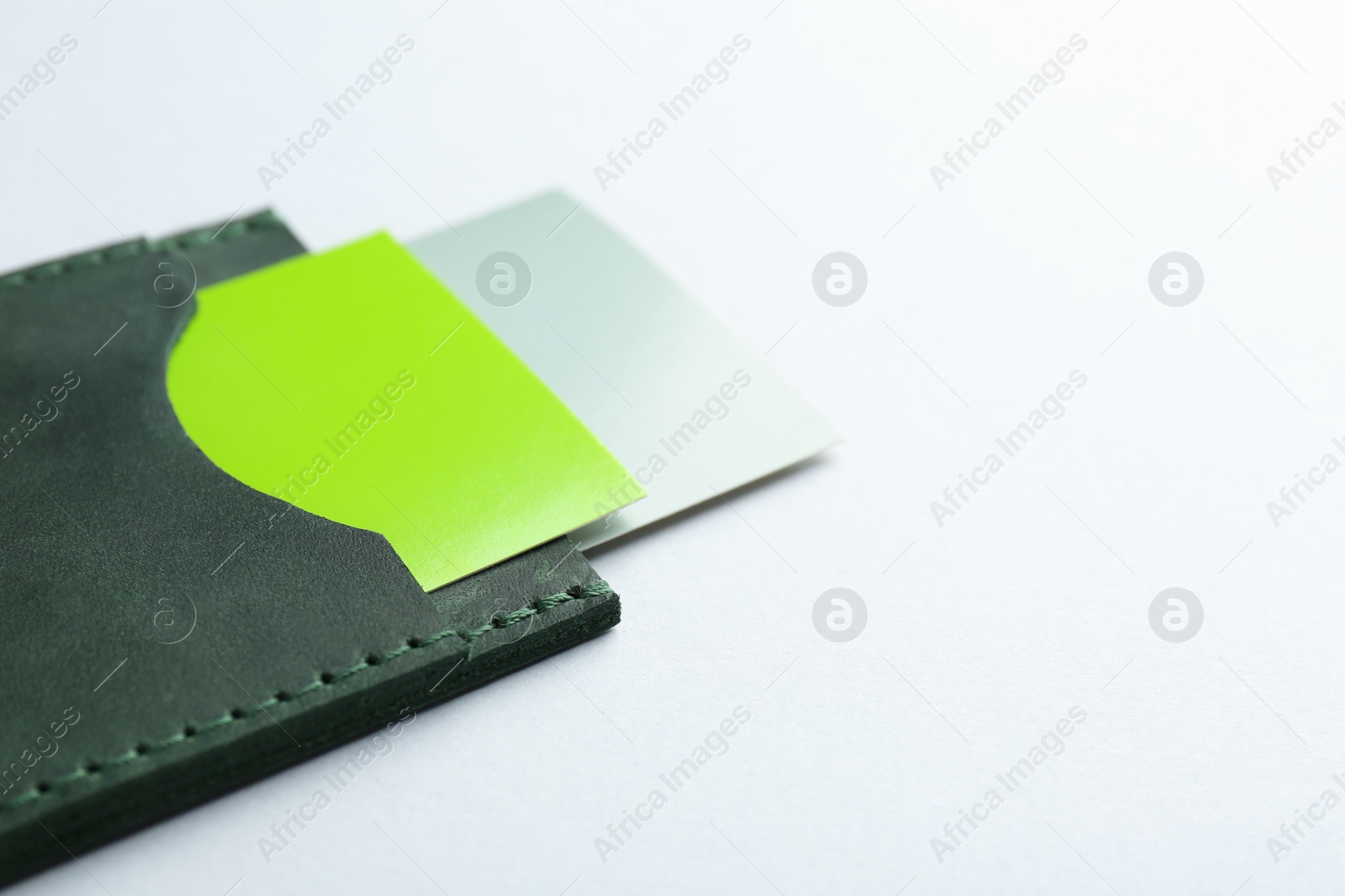 Photo of Leather business card holder with colorful cards on light grey background, closeup. Space for text