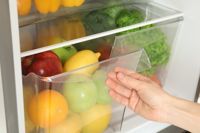 Woman opening refrigerator drawer with fresh fruits, closeup