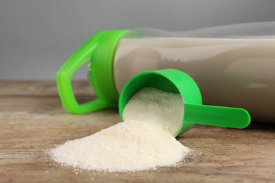 Measuring scoop of protein powder and bottle with shake on wooden table, closeup