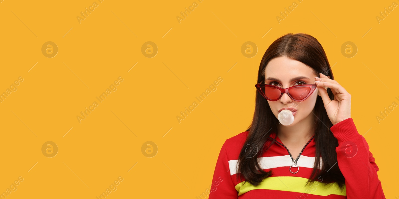 Photo of Beautiful woman in sunglasses blowing bubble gum on orange background, space for text