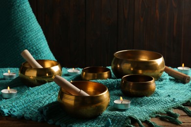 Tibetan singing bowls with mallets, burning candles and turquoise fabric on wooden table