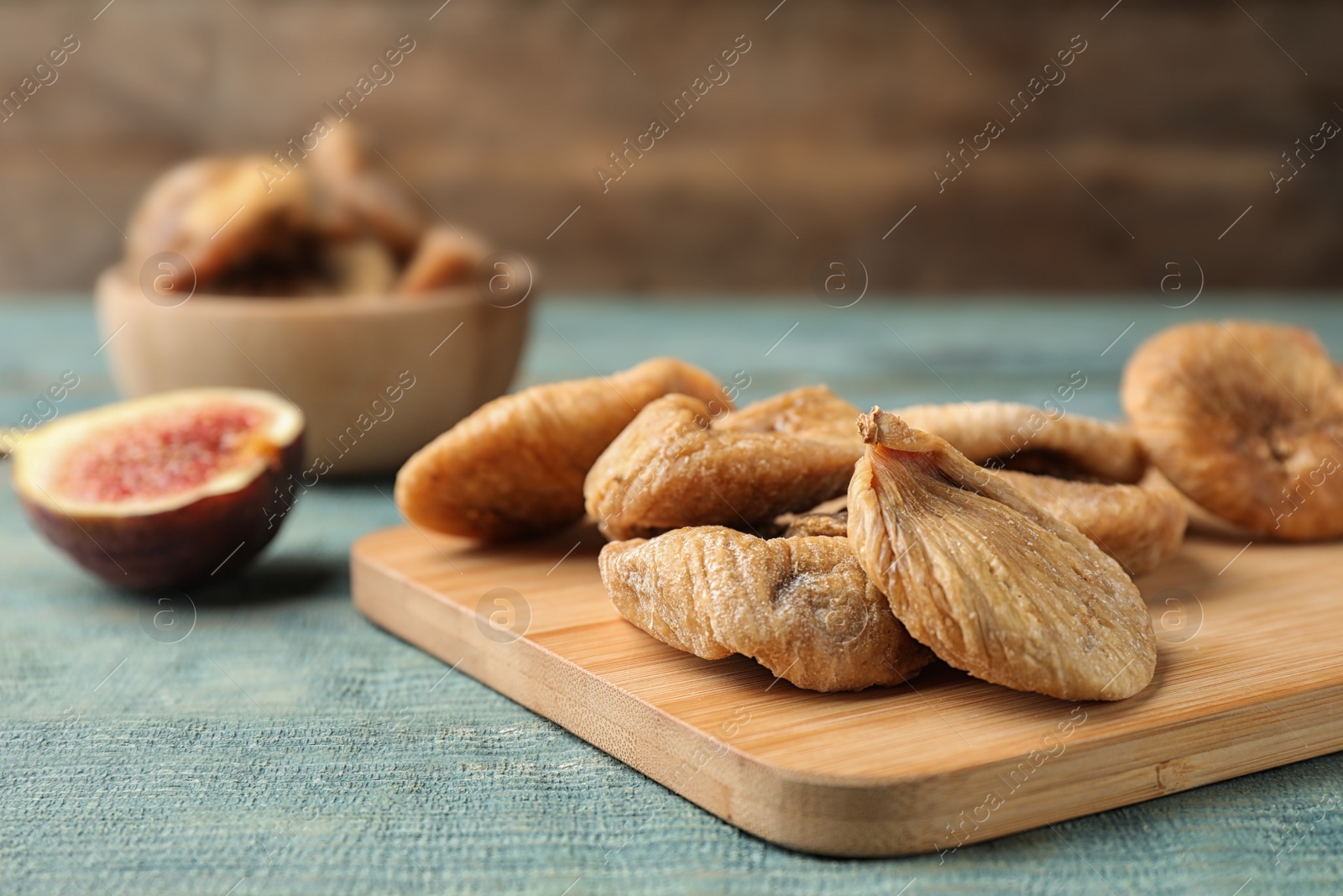 Photo of Wooden board with dried figs on blue table, closeup. Space for text