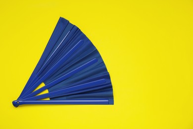 Photo of Bright blue hand fan on yellow background, top view. Space for text