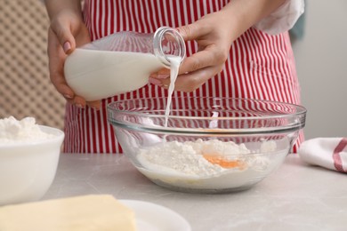Photo of Preparing tasty baklava. Woman pouring milk into bowl with flour and eggs at light grey table, closeup