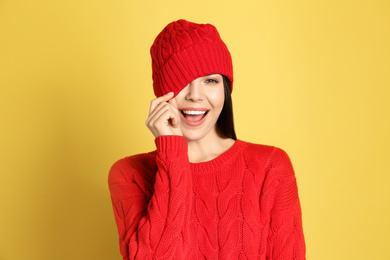 Young woman wearing warm sweater and hat on yellow background. Winter season