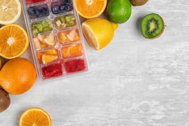 Flat lay composition with ice cube tray and fresh fruits on light background. Space for text