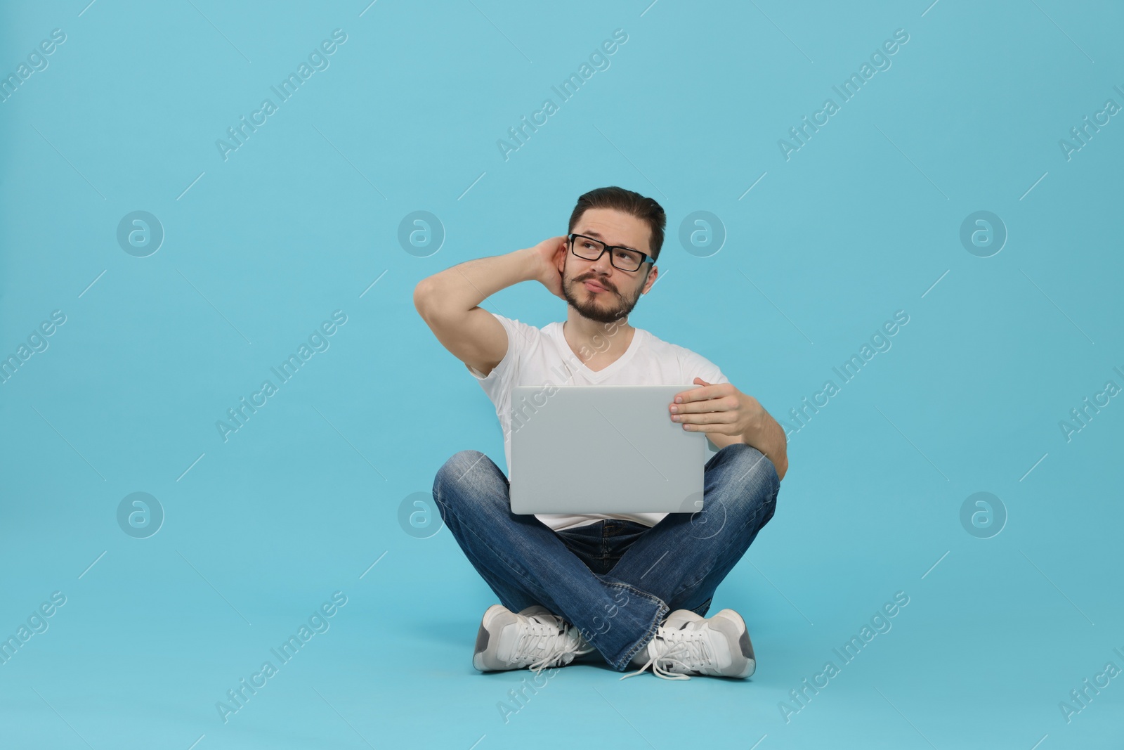Photo of Pensive man sitting and using laptop on light blue background