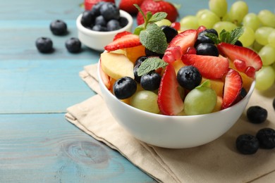 Photo of Tasty fruit salad in bowl and ingredients on light blue wooden table, closeup