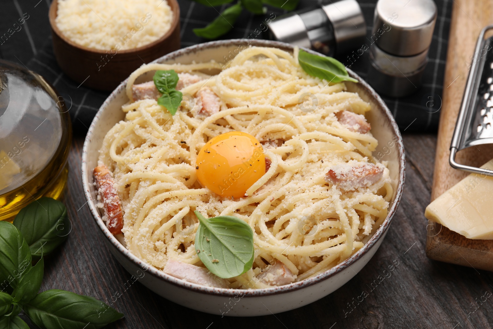 Photo of Bowl of tasty pasta Carbonara with basil leaves and egg yolk on wooden table