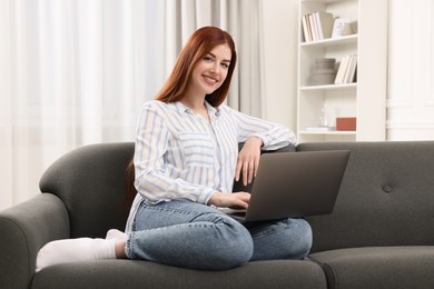 Happy woman with laptop sitting on couch in room