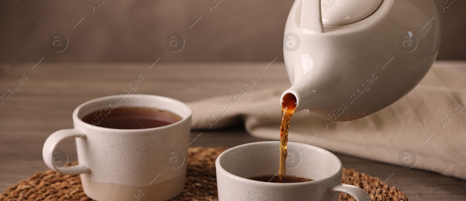 Photo of Pouring aromatic tea into cup at table, closeup