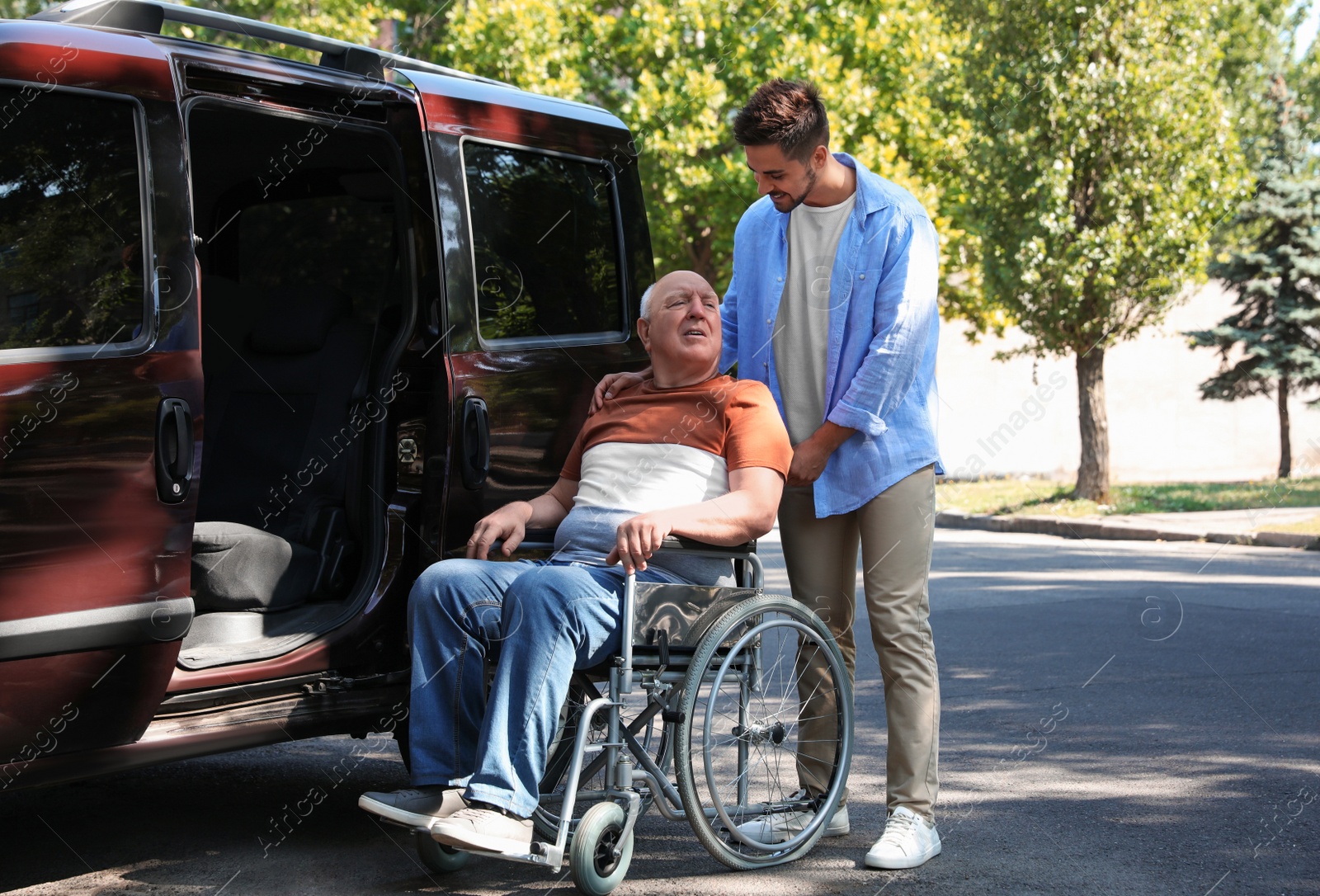 Photo of Young man helping patient in wheelchair to get into van outdoors