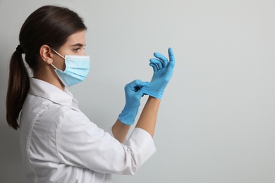 Photo of Doctor in protective mask putting on medical gloves against light grey background. Space for text