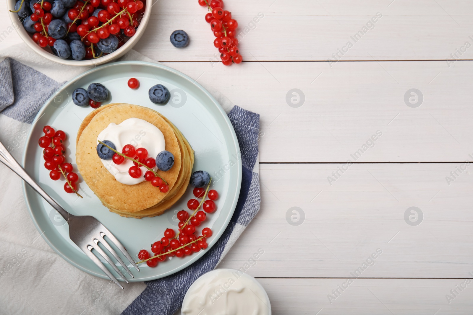 Photo of Tasty pancakes with natural yogurt, blueberries and red currants on white wooden table, flat lay. Space for text