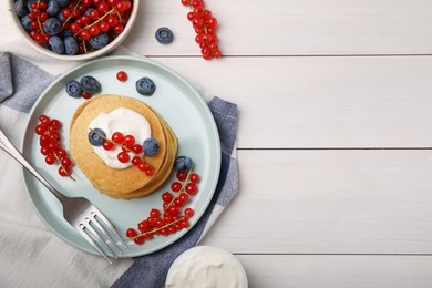 Tasty pancakes with natural yogurt, blueberries and red currants on white wooden table, flat lay. Space for text