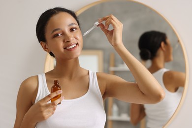 Smiling woman applying serum onto her face in bathroom