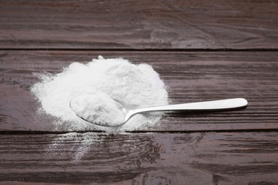 Photo of Spoon and sweet powdered fructose on black wooden table