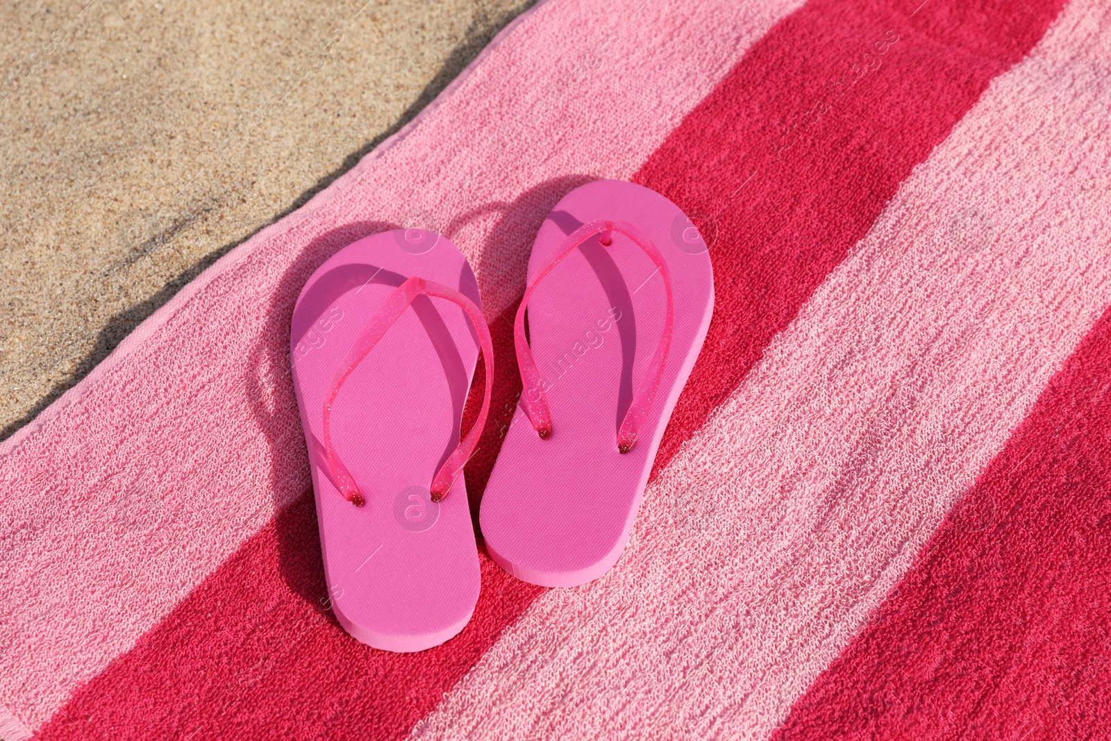 Photo of Beach towel and stylish slippers on sand, above view