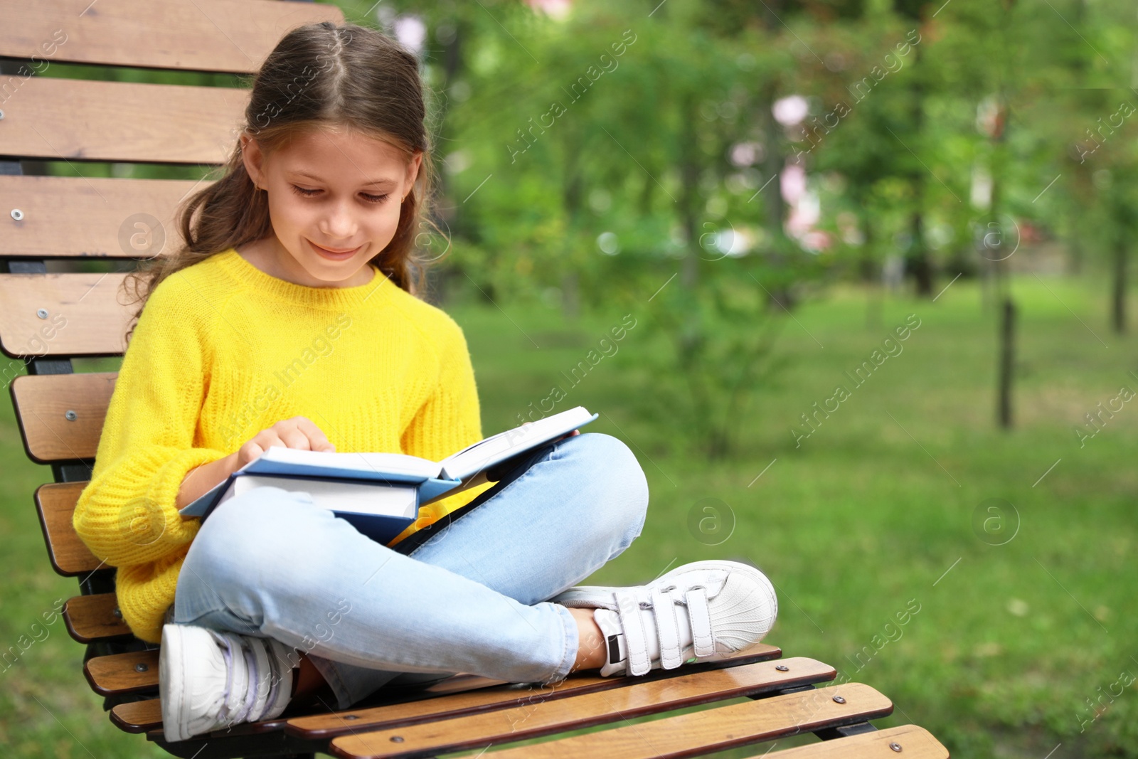 Image of Happy little girl reading book in park 