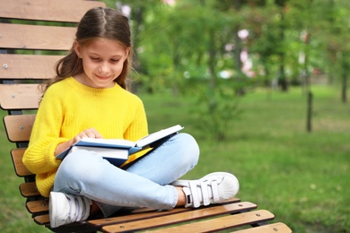 Image of Happy little girl reading book in park 