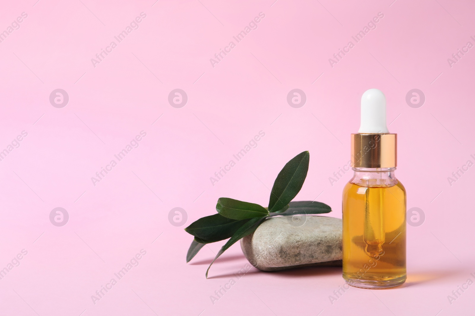 Photo of Bottle with cosmetic oil, green leaves and stone on pink background. Space for text