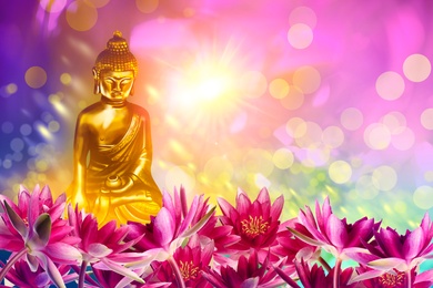 Image of Buddha figure among lotus flowers on bright background, bokeh effect