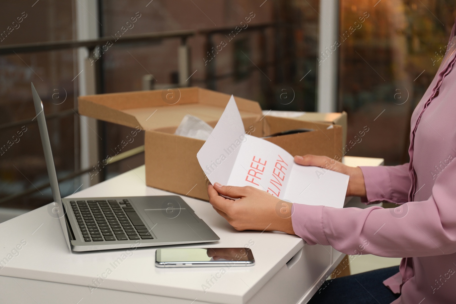 Photo of Woman with note Free Delivery working at table indoors, closeup. Courier service