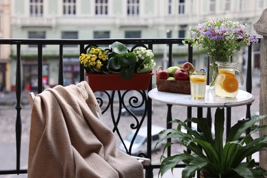 Photo of Relaxing atmosphere. Refreshing drink, apples and beautiful flowers on table near potted houseplants at balcony
