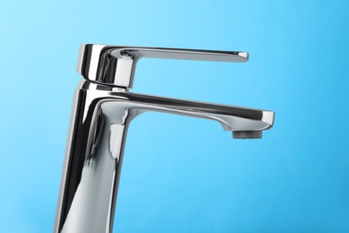 Photo of Single handle water tap on light blue background, closeup